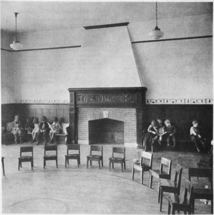A black and white image of chairs in a circle. In the background there is an empty fireplace and people sitting along the wall.