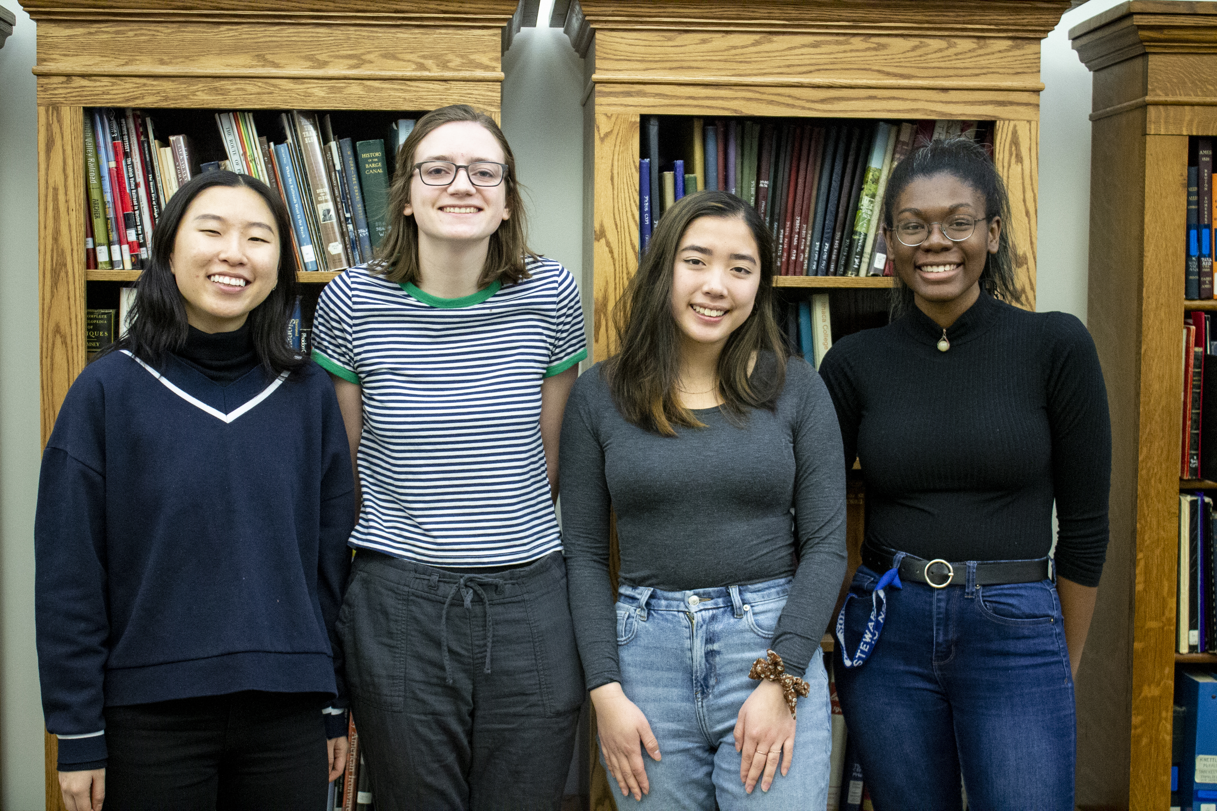 A picture of four students standing in front of a bookcase.