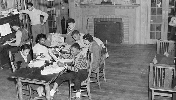 Group of people engaging in various activities in a common area with a piano, fireplace, and table in the southside community center