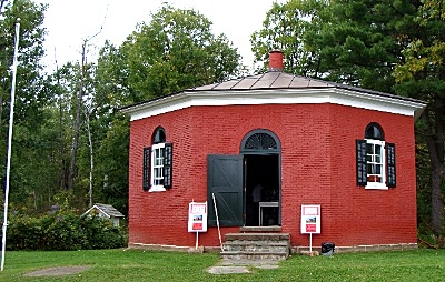 An image of the exterior of the Eight Square Schoolhouse. It is a small red-brick building.