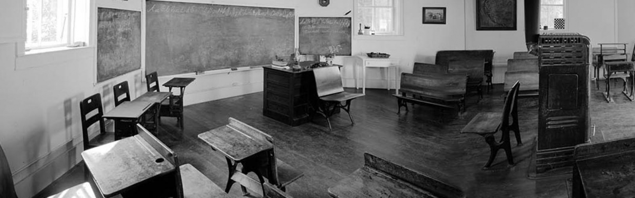 A black and white rectangular image of the classroom inside the schoolhouse.